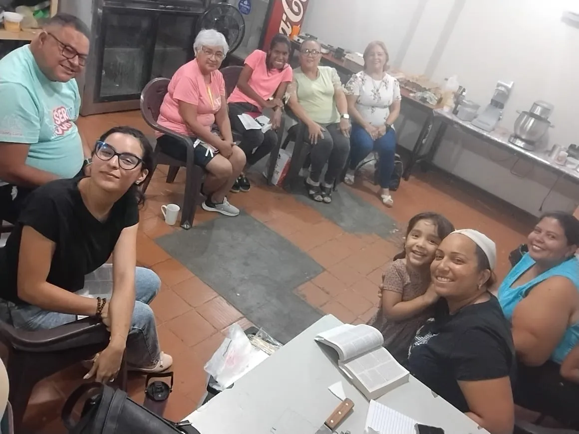 Miembros de una comunidad sonriendo a la cámara, con la Biblia abierta sobre la mesa